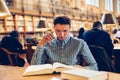 Student man sitting on the desk in library reading room and doing research reading books