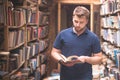 Student portrait of a beard standing in a public library between shelves and looking at a book in his hands Royalty Free Stock Photo