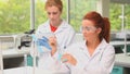 Student pouring liquid while her classmate is taking notes