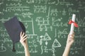 Student raised up arms holding graduation cap and diploma in classroom on green chalkboard