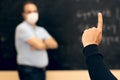 Student raising hand in a class with the teacher wearing face mask looking him upset. Covid situation. New normal