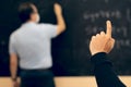 Student raising hand with the teacher wearing face mask writing on the blackboard. Covid situation. New normal. Pandemic