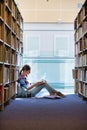 Student reading book while sitting against bookshelf at library Royalty Free Stock Photo