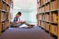 Student reading book while sitting against bookshelf at library Royalty Free Stock Photo