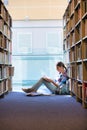 Student reading book while sitting against bookshelf at library Royalty Free Stock Photo