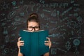 Student reading Open Book hiding Face. Shocked Young Girl in Eyeglasses behind Empty Blue Book Cover over Chalkboard with Math Royalty Free Stock Photo