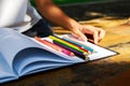 Student`s hand is on the wood table.The crayon is on the white paper.