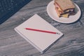 Student`s hard working. Tasty big sandwich on round plate, notebook with pencil, keyboard on gray wooden background. Vintage effe