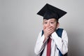 Student scared covered his mouth with his hands. Boy in school uniform and academic hat. White background