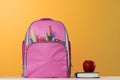 Student set. Pink backpack with office supplies, a book, a red apple on the table on a yellow background. Back to school Royalty Free Stock Photo