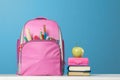 Student set. Pink backpack with stationery, a stack of books, a lunchbox, an apple on the table on a blue background. Back to Royalty Free Stock Photo