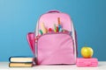 Student set. Pink backpack with stationery, a stack of books, a lunchbox, an apple on the table on a blue background. Back to