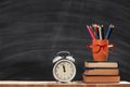 Student set. A stack of books, pencils, an alarm clock, glasses on the background of a school black board. Education concept. Royalty Free Stock Photo
