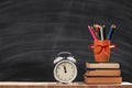 Student set. A stack of books, pencils, an alarm clock, glasses on the background of a school black board. Education concept.