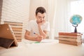 Student sits at the table at the bookside with a pen in his hands. A tired teen does homework at home. Learning the concept