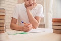 Student sits at the table at the bookside with a pen in his hands. A tired teen does homework at home. Learning the concept