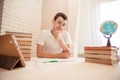 Student sits at the table at the bookside with a pen in his hands. A tired teen does homework at home. Learning the concept