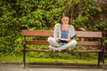 Student sitting on bench listening music with mobile phone and revising Royalty Free Stock Photo