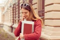 Student smiling shy. Woman holding books smiling hiding face with hand, long hair, casual outfit red burgundy blouse sunglasses on