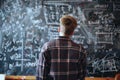 Student solves math problem at blackboard, boy teenager thinks and looks at formulas in class, back view. Concept of child, kid,