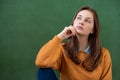 Student thinking and leaning against green chalkboard background. Pensive girl looking up. Caucasian female student portrait. Royalty Free Stock Photo