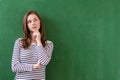 Student thinking and leaning against green chalkboard background. Pensive girl looking up. Caucasian female student portrait.