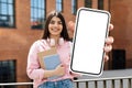 student woman holding books and huge smartphone blank touchscreen outdoors