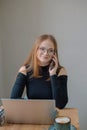 student working remotely. a young woman in a black blouse works on a laptop, talking on the phone and drinking coffee in a cafe. Royalty Free Stock Photo