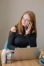 student working remotely. a young woman in a black blouse works on a laptop, talking on the phone and drinking coffee in a cafe. Royalty Free Stock Photo