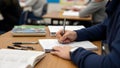 Student writing notes in a classroom with textbooks and notebooks on desk Royalty Free Stock Photo