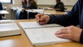 Student writing notes in notebook during class with open book on table Royalty Free Stock Photo