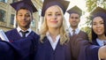 Students in academic regalia taking selfie on graduation day, achievement