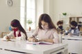 Two elementary school girls wearing handmade face masks sitting at desk and writing Royalty Free Stock Photo