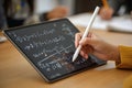 A students hand uses a stylus on a digital tablet, actively solving math equations as part of an online lesson. The setting Royalty Free Stock Photo