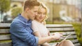 Students in love sitting on bench, using laptop, choosing where to spend summer