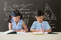 Students at table writing against grey blackboard with education and school graphics Royalty Free Stock Photo