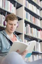 Student reading book while listening music against bookshelf at library Royalty Free Stock Photo