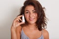 Studio beauty shot of woman with little tube of moisturizing face cream in hands, looking at camera with charming smile, posing