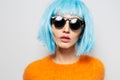 Studio close-up portrait of young girl with blue bob hairstyle, wearing sunglasses and orange sweater on white background Royalty Free Stock Photo