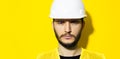 Studio close-up portrait of young serious man architect, builder engineer, wearing white construction safety helmet and yellow jac Royalty Free Stock Photo