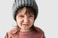 Studio closeup portrait of cute unhappy little girl with grumpy emotion in the winter warm gray hat, wearing sweater isolated on a Royalty Free Stock Photo