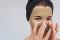 Studio closeup portrait of young woman applying facial cosmetic green clay organic mask on her face, wears black towel on hair. Royalty Free Stock Photo