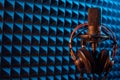 Studio condenser microphone with professional headphones on blue acoustic panel Royalty Free Stock Photo