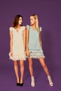 Professional photo of two young women, blonde and brunette, in cocktail dresses posing on purlpe background Royalty Free Stock Photo