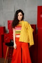 Studio fashion shooting. The girl in a bright outfit, top and pants flared in red and orange tones. Brunette with curly Royalty Free Stock Photo