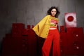 Studio fashion shooting. The girl in a bright outfit, top and pants flared in red and orange tones. Brunette with curly Royalty Free Stock Photo