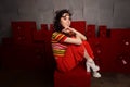 Studio fashion shooting.The girl in a bright outfit, top and pants flared in red and orange tones. Brunette with curly Royalty Free Stock Photo