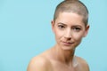 Studio headshot portrait of a beautiful young caucasian woman with shaved head against pastel blue background. Cancer survivor.