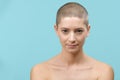 Studio headshot portrait of a beautiful young caucasian woman with shaved head against pastel blue background. Cancer survivor.