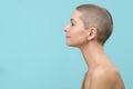 Studio headshot portrait of a beautiful young caucasian woman with shaved head against pastel blue background. Cancer survivor.